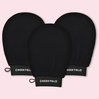 A set of three CheekyGlo Exfoliating Gloves in black are displayed against a light pink background, each featuring the "CheekyGlo" brand name in white on the wristband. These gloves are designed to help you achieve smoother, healthier skin with every use.