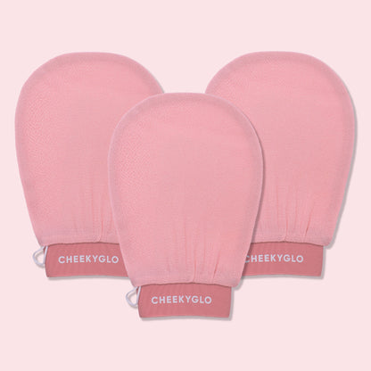 Three CheekyGlo Exfoliating Gloves are displayed against a light pink backdrop. The gloves are slightly rounded at the top with elasticated wristbands labeled "CHEEKYGLO," promising smoother skin and a healthier glow.