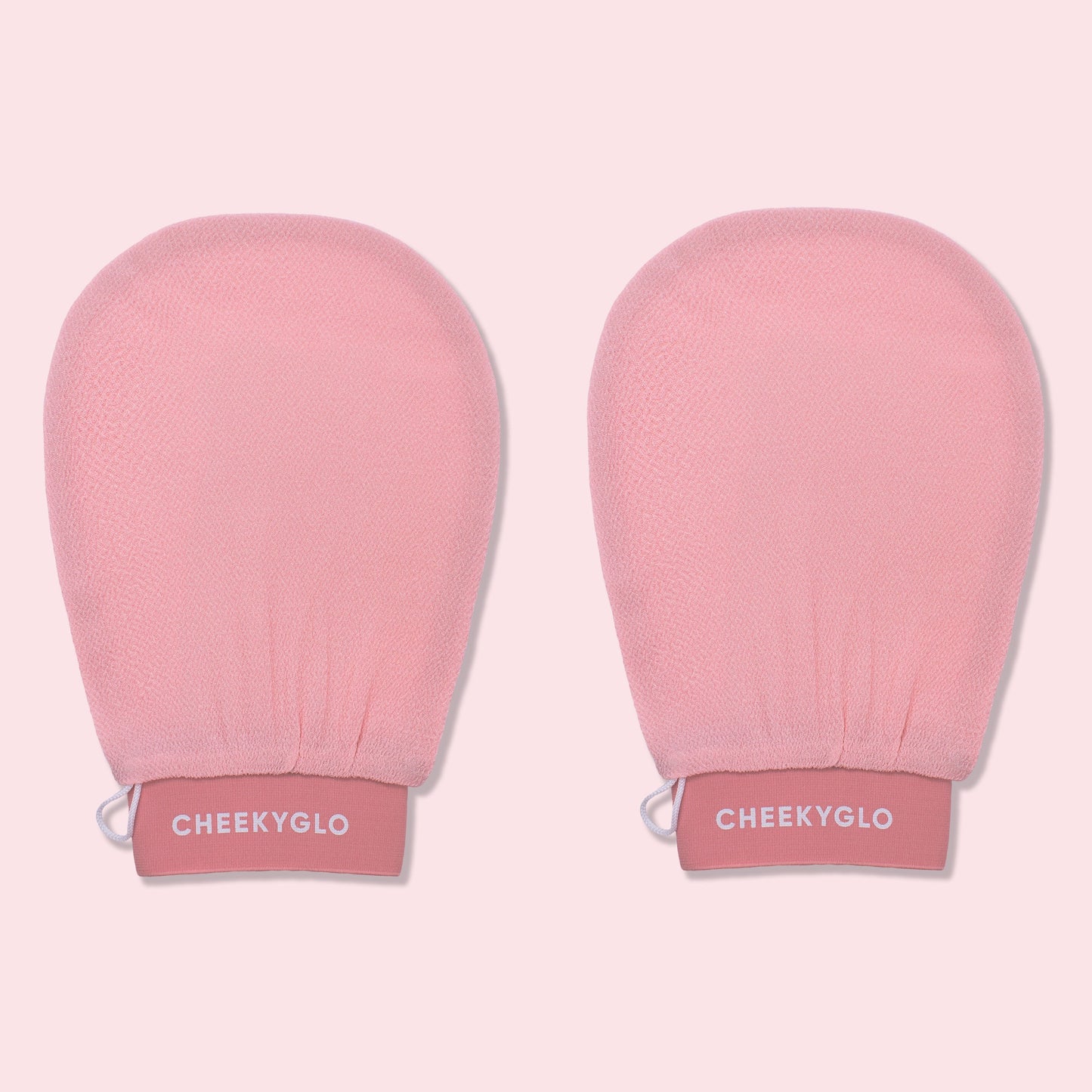 Two pink CheekyGlo Exfoliating Gloves with "CheekyGlo" printed in white on the wristbands. The gloves promise smoother, healthier skin and are set against a light pink background.