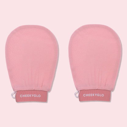 Two pink CheekyGlo Exfoliating Gloves with "CheekyGlo" printed in white on the wristbands. The gloves promise smoother, healthier skin and are set against a light pink background.